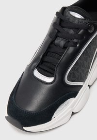 Black and white leather and suede sneaker with black laces, white sole, and Michael Kors logo on side and tongue.