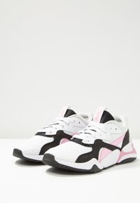 White sports sneakers with black and pink accents, laced up, angled side view on a white surface and neutral background.
