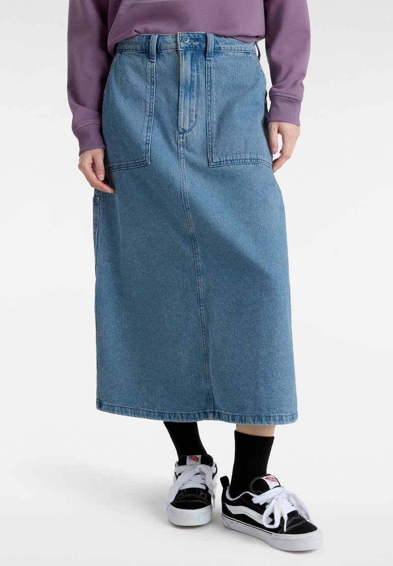 Jupe midi en denim bleu avec de grandes poches devant, portée avec des chaussettes noires et des baskets noir et blanc, associée à un haut violet à manches longues.