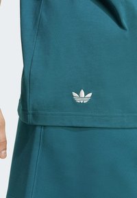 Tükil värviga sportlik topp sujuva tekstuuriga. Erakordne valge brodeeritud kolme lehe logo alläärmisel ja lõdva istuvusega.