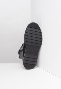 Botte en cuir noir présentée par le bas, avec une semelle en caoutchouc texturée et des rainures horizontales pour l'adhérence, ainsi qu'une fermeture à glissière sur le côté.