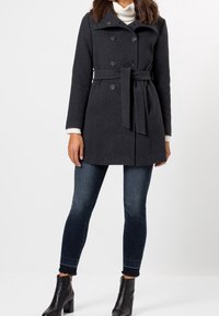 Abrigo de doble faz gris oscuro con cinturón, hecho de una mezcla de lana texturizada. Combinado con vaqueros azules y botines negros de tacón.