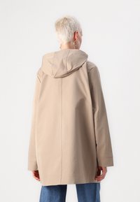 Cappotto impermeabile beige con cappuccio, caratterizzato da un taglio dritto, maniche lunghe e dettagli di cuciture sottili; la texture è liscia e opaca.