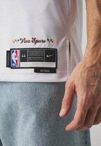 Camiseta blanca de la NBA con el texto "Viva Spurs", detalles de la etiqueta incluyendo "ENGINEERED", tamaño 44 y logo de Nike. La tela presenta una textura de malla.