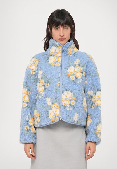 Veste polaire bleue avec motif floral orange et blanc, dotée d'un col montant, d'une fermeture éclair et d'un tissu à texture douce.