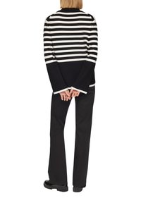 Gestreifter schwarz-weißer Pullover mit weitem Ausschnitt und ausladenden Ärmeln, kombiniert mit schwarzen Hosen und klobigen schwarzen Schuhen.
