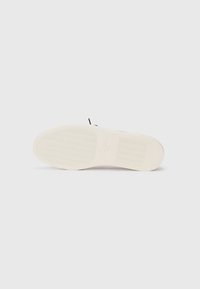 Semelle d'une sneaker blanche avec un motif de grip beige clair, posée à plat sur un fond blanc avec un texte de marque discret au centre.