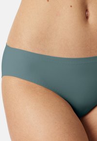 Green bikini bottom with a smooth texture, low-rise design, and minimal stitching. Close-up view, highlighting the color and shape.