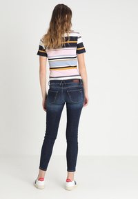 Jeans ajustados de color azul oscuro con una cintura de altura media, que presentan un diseño tradicional de cinco bolsillos y una pequeña etiqueta de la marca en la parte trasera.