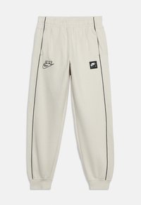 Lys beige Nike Air joggebukser med svart piping, elastisk midjebånd og mansjetter, svarte Nike Air logoer på fremre lår.