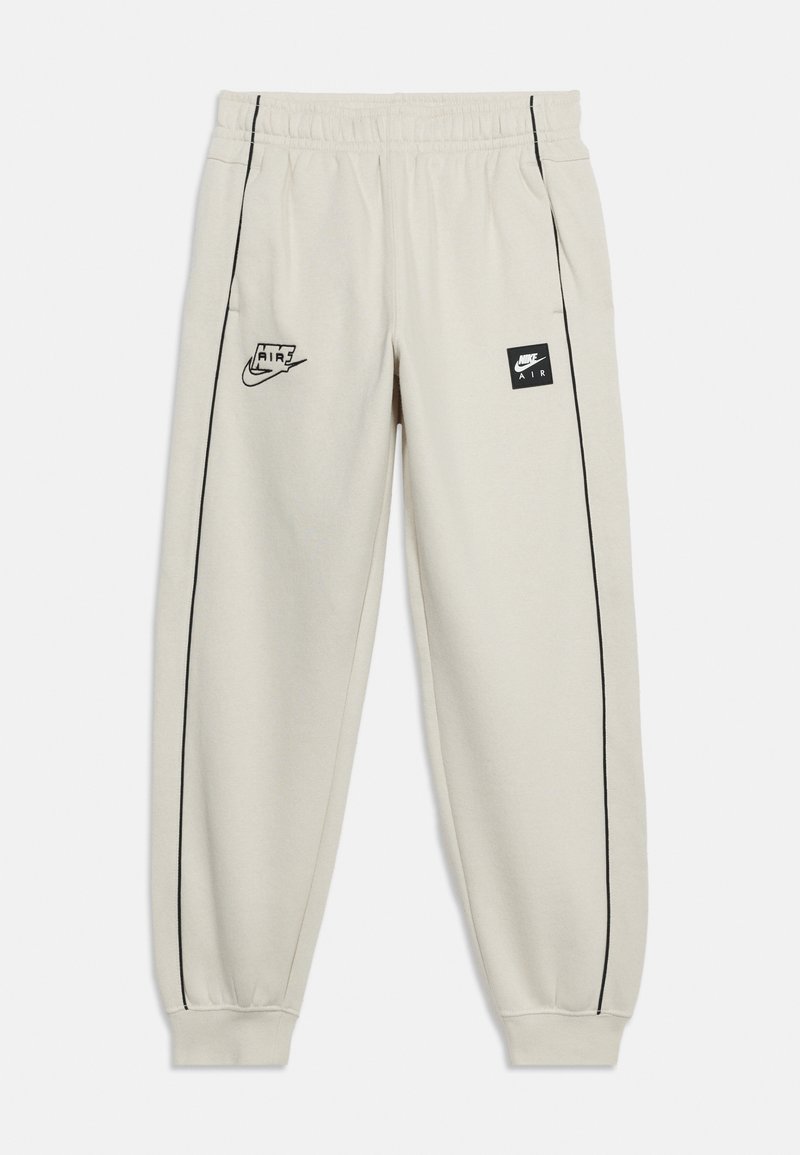 Lys beige Nike Air joggebukser med svart piping, elastisk midjebånd og mansjetter, svarte Nike Air logoer på fremre lår.
