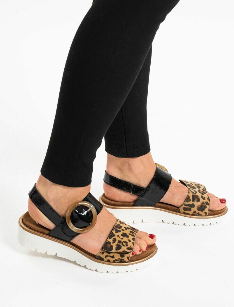 Open-toe sandalen met een leopardsupport, zwarte lakleren accenten, een cirkelvormig hardware detail en een witte platformzool.
