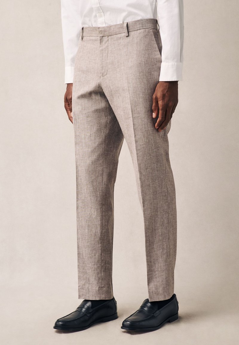 Világosbarna lenvászon nadrág, szabott fazonú, sík elejű, oldalzsebekkel és övcsíptetőkkel, fekete mokaszinnal párosítva.