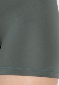 Pantalones cortos deportivos de color verde oscuro, hechos de una tela elástica. Textura suave con un ajuste ceñido y un dobladillo cosido de contraste.