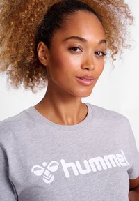 Grå t-shirt med korte ærmer, med et hvidt "hummel" logo og grafisk design. Blød bomuldsstruktur, rund hals.