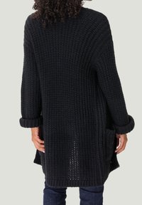 Fetter schwarzer Strickcardigan mit langen Ärmeln, umgeschlagenen Bündchen und vorderen Taschen. Strukturierten Stoff mit einem lockeren, oversized Schnitt.