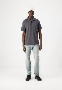 Grijze polo met een kraag, voorzien van een klein logo. Gemaakt in combinatie met lichtblauwe jeans en zwarte sneakers. Afgerond met een beige pet.