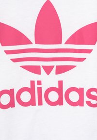 Pink Adidas trefoil logo and brand name printed on white fabric. The logo features three leaf shapes and horizontal stripes.