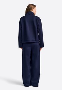 Granatowy sweatshirt z wysokim kołnierzem i luźnym krojem, zestawiony z szerokimi granatowymi spodniami. Gładka faktura, minimalistyczny design.