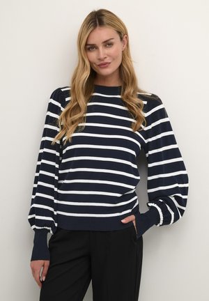 Pull rayé bleu marine et blanc avec un col rond et des manches bouffantes, en tissu doux. Associé à un pantalon noir.