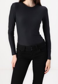 Black long-sleeve top in a smooth, stretchy material paired with high-waisted black jeans featuring button closure and five-pocket design.