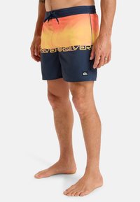 Simshorts i gradient orange och marinblå, med dragsko i midjan, logotryck fram och en patchlogga nedtill.