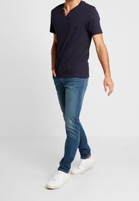 Námořnická krátká rukávová henley košile s třemi knoflíkovými detaily, v kombinaci se světlými modrými slim-fit džíny a bílými teniskami.