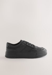 Sneakers basses en cuir noir avec semelle épaisse, fermeture à lacets à l'avant, et détails de couture minimaux sur un fond clair uni.