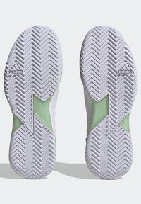 Białe buty sportowe z zielonymi akcentami, posiadające wzór żebrowania na podeszwie oraz logo Adidas na każdym obcasie.