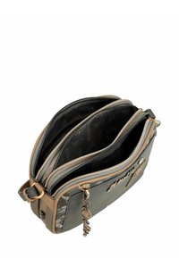 Bolso cruzado gris hecho de cuero sintético con detalles en marrón. Cuenta con tres compartimentos con cremallera y un llavero decorativo. Superficie texturizada.