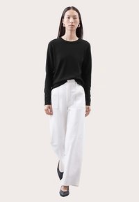 Czarny sweter z długim rękawem i białe spodnie o szerokich nogawkach. Sweter ma okrągły dekolt, spodnie mają przednie kieszenie i prosty krój.