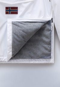 Biała kurtka z naszywką norweskiej flagi; zamykana kieszeń odsłania miękką szaro-skalną podszewkę. Gładki zewnętrzny materiał i schludny design.