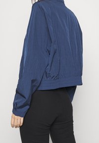 Granatowa krótka kurtka wykonana z lekkiego materiału o pogniecionej fakturze, z elastycznym wykończeniem u dołu i na mankietach oraz stojącym kołnierzem.