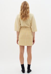 Bežinė megzta palaidinė su trimis ketvirtadaliais rankovėmis; geltona ir balta šachmatų rašto mini sijonas. Ava blackos ir batai.