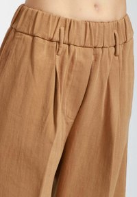 Pantaloni in corduroy marrone chiaro con una finitura testurizzata, dotati di una cintura elastica e pieghe frontali per una maggiore struttura.