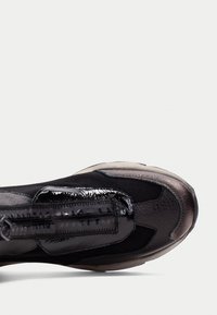 Czarno-szare trampki o smukłej sylwetce, z błyszczącym wykończeniem, fakturowanymi materiałami, widocznymi szwami oraz detalem zamka błyskawicznego.