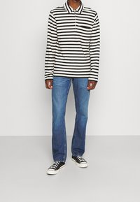 Camisa de polo de manga larga a rayas blancas y negras con cuello, combinada con pantalones vaqueros de mezclilla azul y zapatillas negras.
