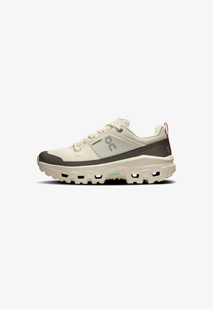 Lightweight beige sneakers with a textured fabric upper, dark brown accents, rubber sole, and a red pull tab on the heel.