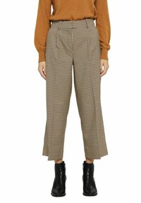 Rutig vida byxor i brunt och svart, med veck, hög midja och kort längd, kombinerat med svarta ankelstövlar.