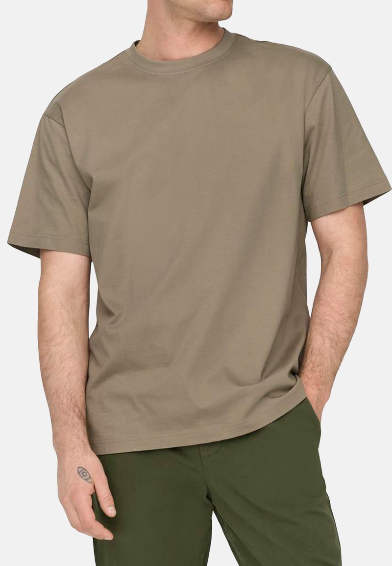 Korte mouwen, ronde hals T-shirt in kaki katoen. Glad textuur, ontspannen pasvorm. Gecombineerd met donkergrijze broek. Geen zichtbare patronen of logo's.