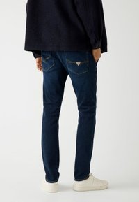 Ciemnoniebieskie dżinsy o slim fit, z teksturowanym wykończeniem, żółtymi przeszyciami oraz trójkątnym logo na tylnej kieszeni.