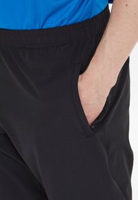 Zwarte sportieve broeken van rekbaar materiaal, met een elastische tailleband en zijzakken. Gladde textuur met een slim-fit ontwerp.