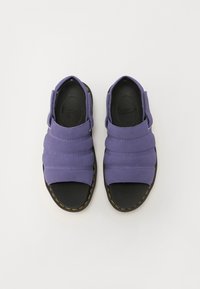 Lilla slip-on sandaler har en polstret overdel med horisontale sømmer og en solid svart såle, akzentuert med gule sting langs kantene.