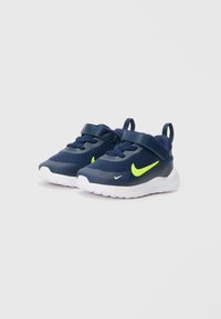 Marineblaue Mesh-Sneaker mit einem gelben Swoosh, ausgestattet mit einem gepolsterten Kragen, einem verstellbaren Riemen und einer weißen Gummisohle.