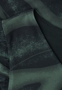 Tissu en maille vert foncé et noir avec un motif subtil de feuilles et des coutures et plis visibles.