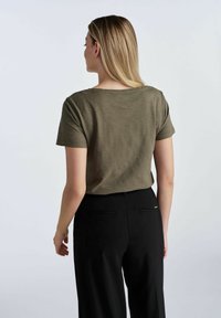 Olive-green T-shirt z krótkim rękawem o swobodnym kroju i okrągłym dekoltem, w zestawie z czarnymi spodniami z kieszeniami. Gładka faktura.