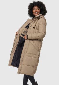 Beige gevoerde jas met een capuchon, voorzien van een rits- en knoopsluiting, grote voorzakken en een contrasterende zwarte voering. Lange, iets oversized pasvorm.