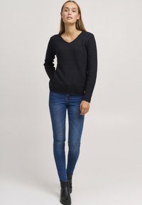 Zwarte V-hals trui met een textuurpatroon, lange mouwen en geribbelde zoom, gecombineerd met blauwe skinny jeans en zwarte enkellaarsjes.