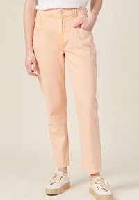 Pantalones de denim melocotón claro con corte recto, con bolsillos delanteros y costuras visibles, combinados con zapatillas blancas sobre un fondo neutro.