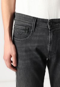 Jeansi negri din denim cu o croială dreaptă, având o mică buzunar frontal, închidere cu nasture și o decolorare subtilă pe picioare.